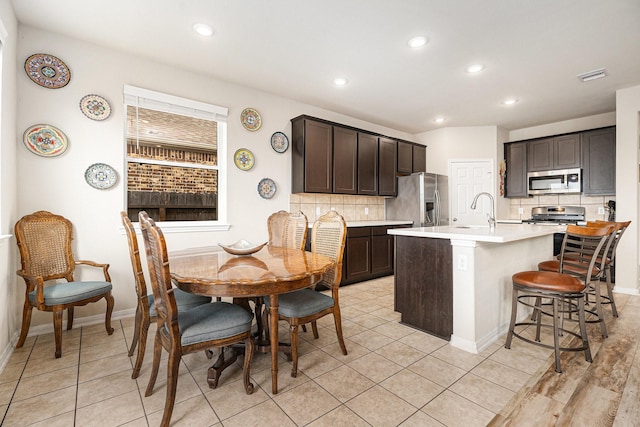 kitchen with tasteful backsplash, an island with sink, a kitchen bar, stainless steel appliances, and dark brown cabinets