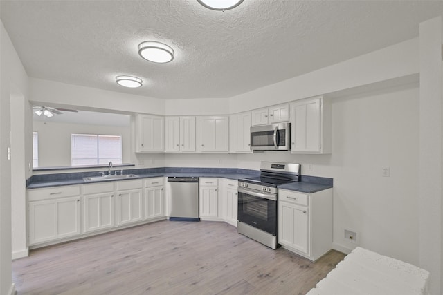 kitchen featuring appliances with stainless steel finishes, sink, white cabinets, and light wood-type flooring