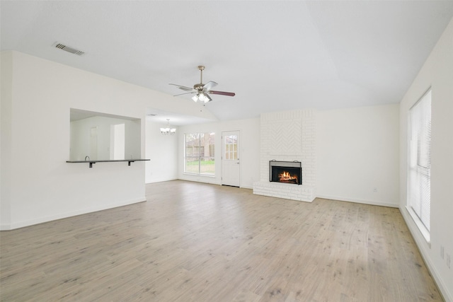 unfurnished living room with a brick fireplace, ceiling fan with notable chandelier, lofted ceiling, and light hardwood / wood-style floors