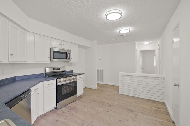 kitchen featuring appliances with stainless steel finishes, light wood-type flooring, a textured ceiling, and white cabinets