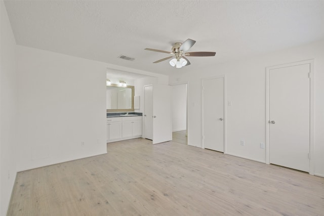 unfurnished bedroom featuring ceiling fan, light hardwood / wood-style floors, a textured ceiling, and ensuite bathroom