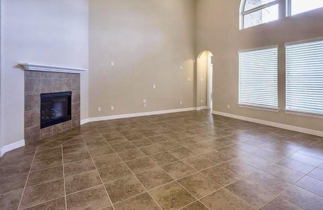 unfurnished living room featuring a fireplace, dark tile patterned floors, and a high ceiling