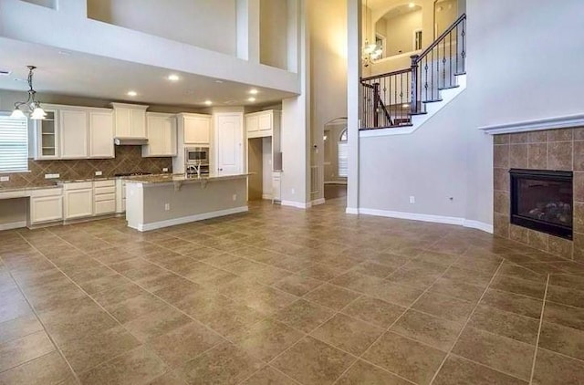 kitchen featuring stainless steel microwave, white cabinetry, a tiled fireplace, a notable chandelier, and a center island with sink