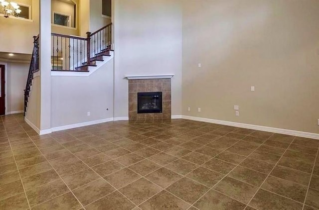 unfurnished living room with a towering ceiling, a fireplace, dark tile patterned floors, and a notable chandelier