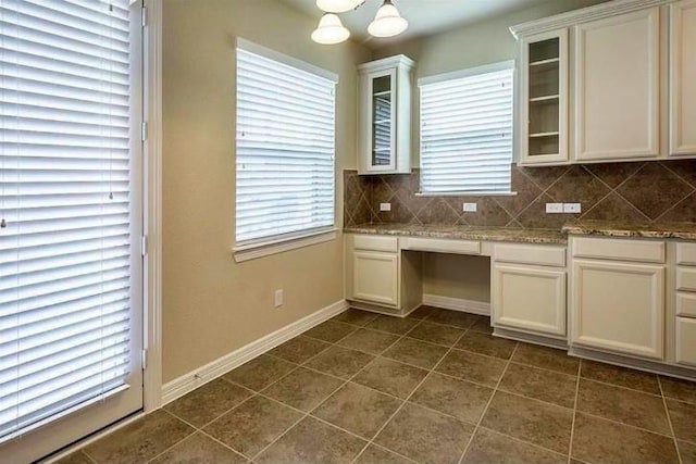 kitchen with built in desk, white cabinets, decorative backsplash, dark tile patterned floors, and light stone countertops