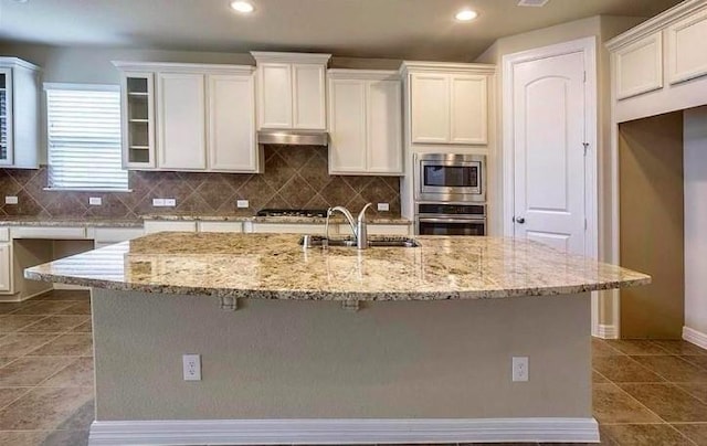 kitchen featuring a kitchen island with sink, sink, light stone countertops, and appliances with stainless steel finishes