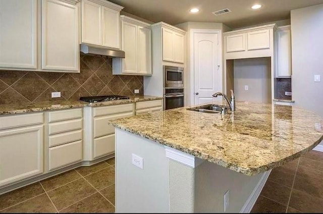 kitchen with stainless steel appliances, light stone countertops, a kitchen island with sink, and sink