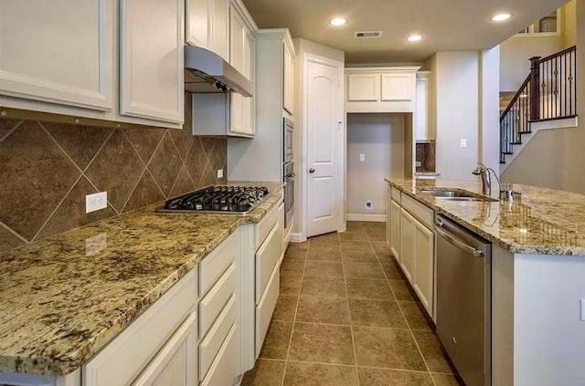 kitchen with dark tile patterned floors, appliances with stainless steel finishes, white cabinetry, light stone counters, and decorative backsplash