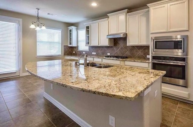 kitchen featuring a center island with sink, white cabinets, pendant lighting, stainless steel appliances, and backsplash