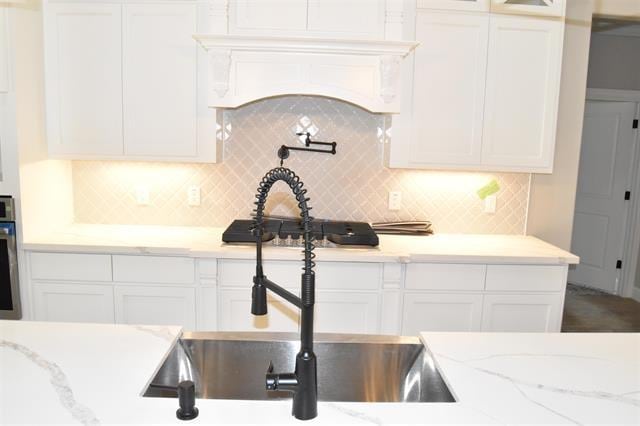 kitchen featuring light stone counters, sink, decorative backsplash, and white cabinets