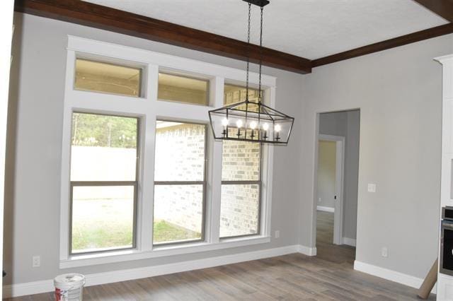 unfurnished dining area with hardwood / wood-style flooring, crown molding, a chandelier, and beamed ceiling