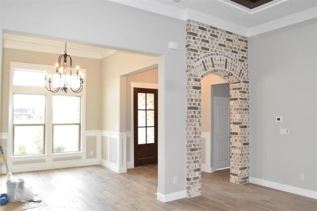 interior space featuring an inviting chandelier, wood-type flooring, ornamental molding, and a healthy amount of sunlight