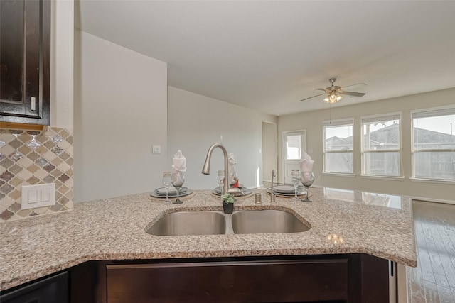 kitchen with dark brown cabinetry, a healthy amount of sunlight, light stone countertops, and sink