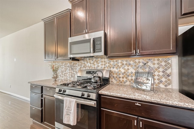 kitchen featuring dark brown cabinetry, appliances with stainless steel finishes, light stone countertops, and decorative backsplash