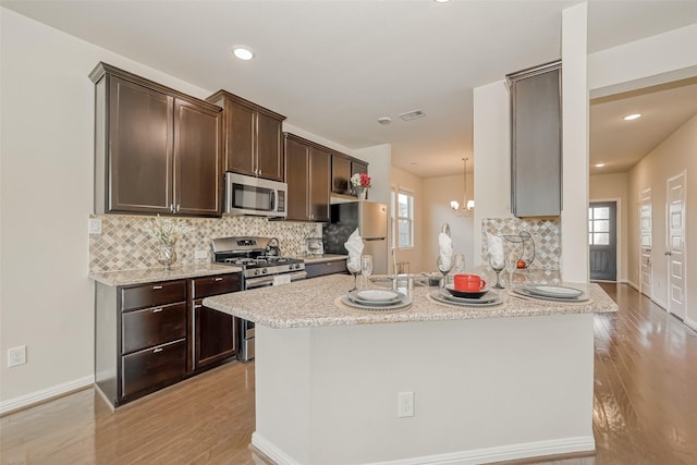 kitchen with appliances with stainless steel finishes, backsplash, kitchen peninsula, light stone countertops, and light hardwood / wood-style flooring