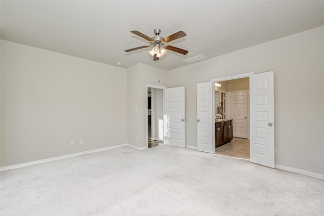 unfurnished bedroom featuring ceiling fan, light colored carpet, and ensuite bath