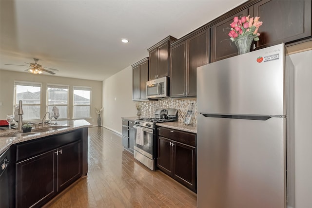 kitchen featuring appliances with stainless steel finishes, sink, decorative backsplash, dark brown cabinetry, and light hardwood / wood-style flooring