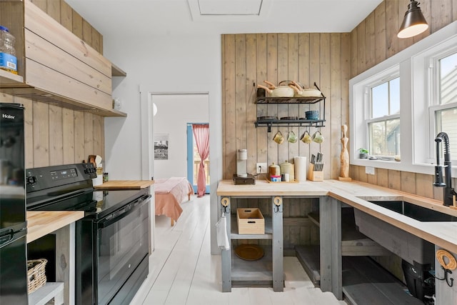 kitchen with sink, wood walls, light wood-type flooring, range hood, and black appliances