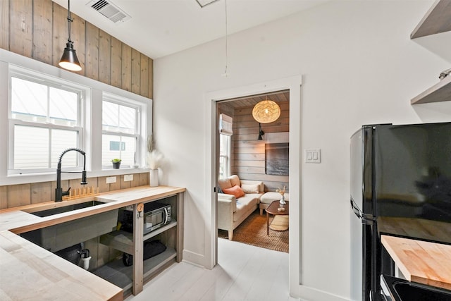 kitchen featuring black refrigerator, wood counters, wood walls, decorative light fixtures, and sink