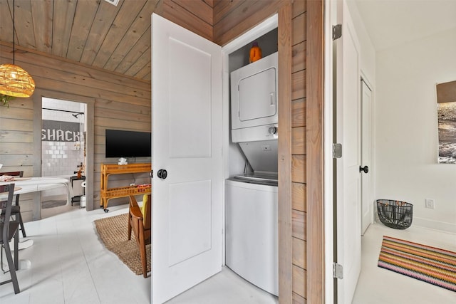 laundry area featuring stacked washer and clothes dryer, wooden walls, and wooden ceiling