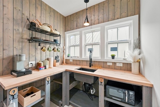 interior space with decorative light fixtures, butcher block counters, sink, and wood walls