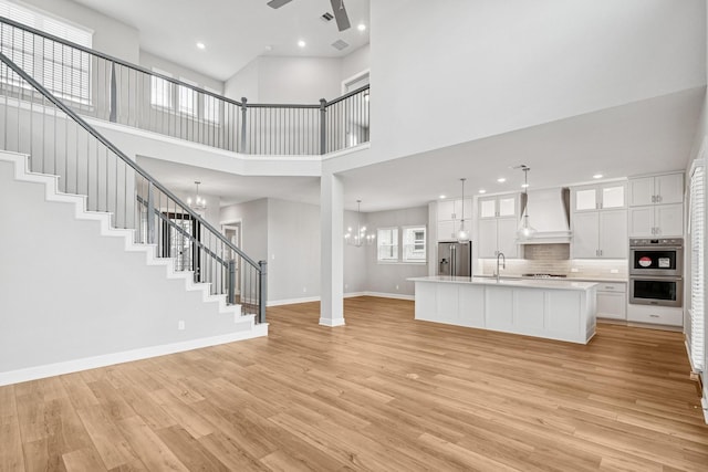 20406 Magnolia Flint Dr, Cypress, TX 77433 - unfurnished living room featuring a chandelier, light wood-style floors, a towering ceiling, stairway, and a ceiling fan