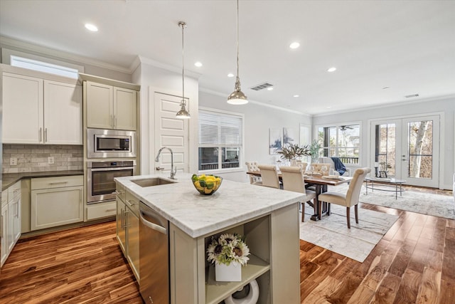 kitchen featuring decorative light fixtures, an island with sink, sink, light stone counters, and stainless steel appliances