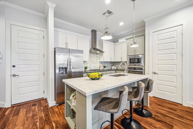 kitchen featuring sink, hanging light fixtures, a kitchen island with sink, stainless steel appliances, and wall chimney range hood