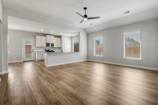 unfurnished living room with ceiling fan, vaulted ceiling, sink, and light wood-type flooring