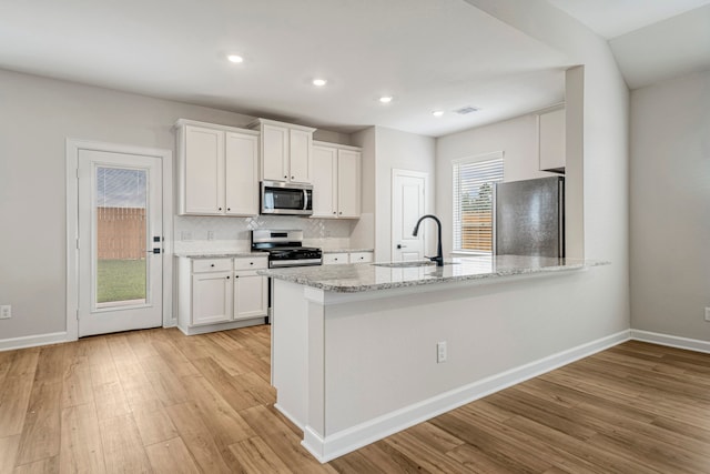 kitchen with appliances with stainless steel finishes, tasteful backsplash, white cabinetry, sink, and light stone counters