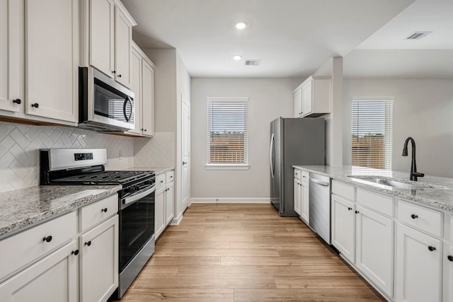 kitchen featuring sink, white cabinetry, tasteful backsplash, stainless steel appliances, and light stone countertops