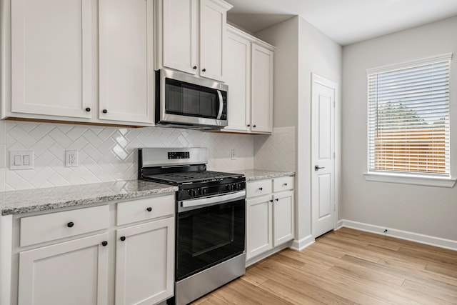 kitchen with light hardwood / wood-style flooring, appliances with stainless steel finishes, white cabinetry, backsplash, and light stone counters