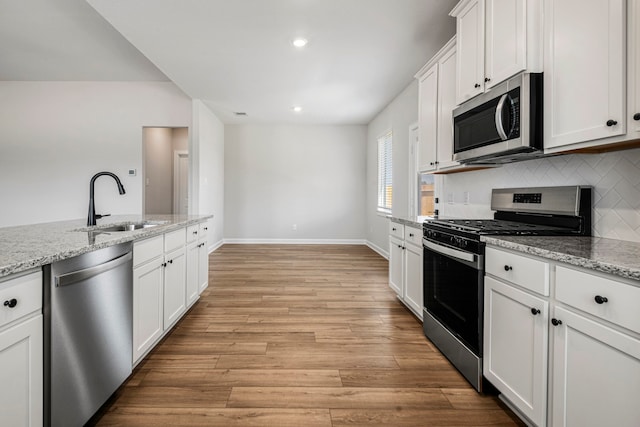 kitchen with sink, light hardwood / wood-style flooring, white cabinetry, stainless steel appliances, and light stone counters