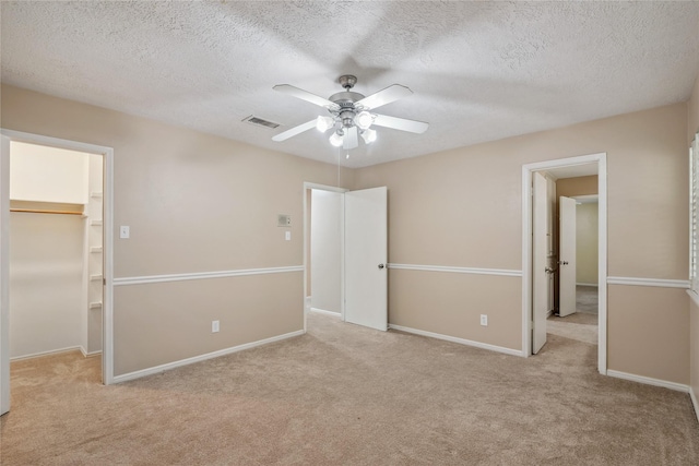 unfurnished bedroom featuring ceiling fan, a textured ceiling, a walk in closet, light colored carpet, and a closet