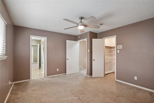 unfurnished bedroom with ensuite bathroom, a spacious closet, ceiling fan, light carpet, and a textured ceiling