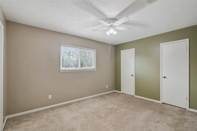 unfurnished bedroom with multiple closets, ceiling fan, light carpet, and a textured ceiling