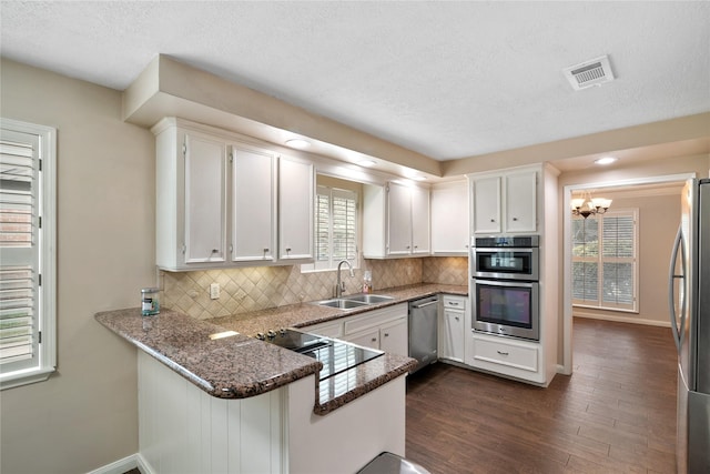 kitchen featuring sink, stainless steel appliances, kitchen peninsula, white cabinets, and dark stone counters