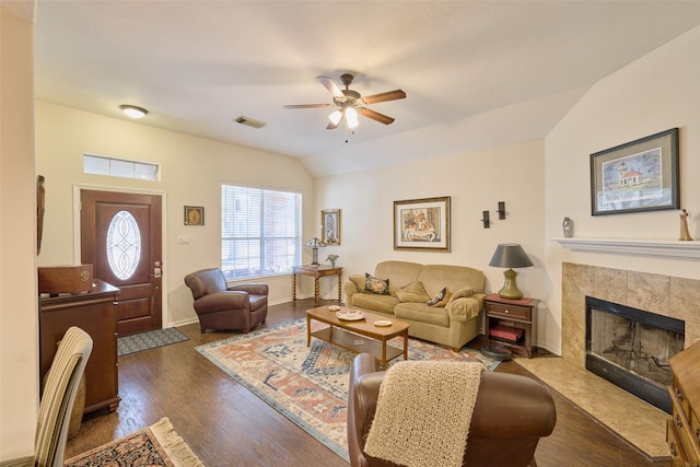 living room with dark wood-type flooring, lofted ceiling, a tile fireplace, and ceiling fan