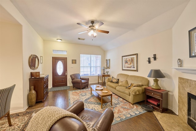 living room with light wood-type flooring, a tile fireplace, vaulted ceiling, and ceiling fan