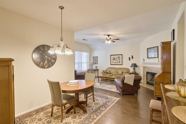 dining area featuring ceiling fan with notable chandelier, a tiled fireplace, dark wood-type flooring, and lofted ceiling