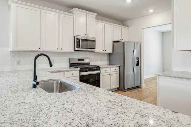 kitchen featuring stainless steel appliances, light stone countertops, sink, and white cabinets