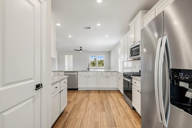 kitchen with sink, white cabinetry, appliances with stainless steel finishes, light stone countertops, and light hardwood / wood-style floors