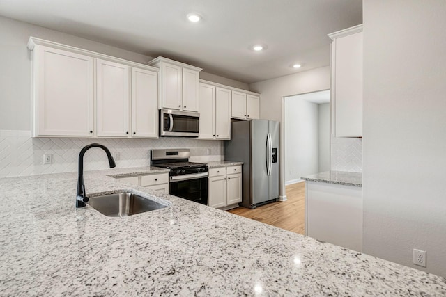 kitchen featuring sink, appliances with stainless steel finishes, backsplash, light stone counters, and white cabinets