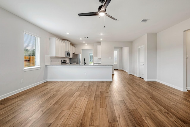 kitchen featuring tasteful backsplash, kitchen peninsula, stainless steel appliances, light hardwood / wood-style floors, and white cabinets