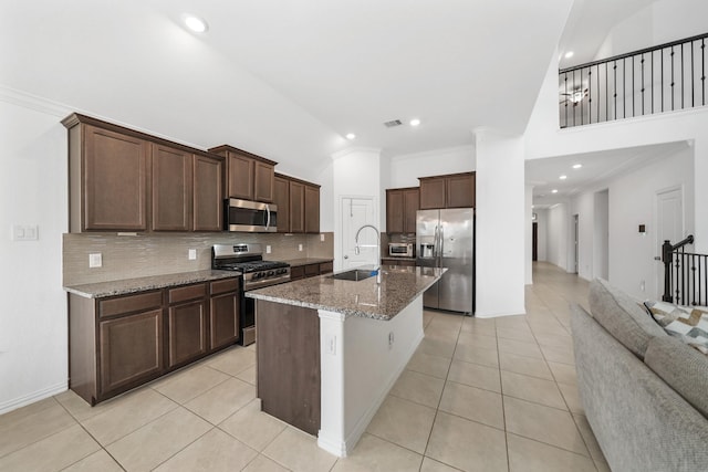 kitchen with sink, light tile patterned floors, stainless steel appliances, light stone counters, and an island with sink