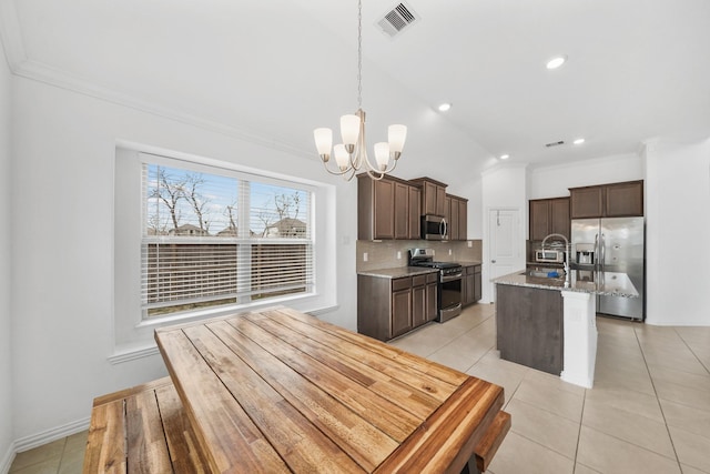 kitchen with sink, light stone counters, pendant lighting, stainless steel appliances, and a kitchen island with sink