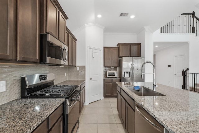 kitchen with sink, light tile patterned floors, appliances with stainless steel finishes, dark brown cabinets, and light stone countertops