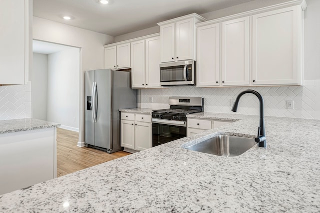 kitchen featuring sink, light hardwood / wood-style flooring, appliances with stainless steel finishes, white cabinetry, and light stone counters