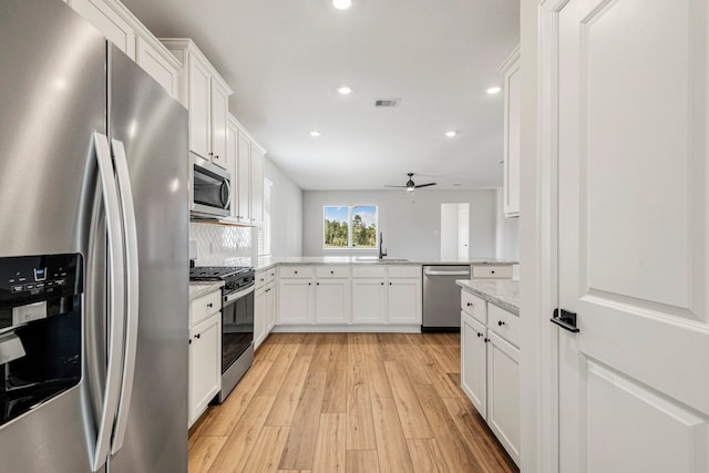 kitchen featuring sink, white cabinetry, light stone counters, stainless steel appliances, and light hardwood / wood-style floors