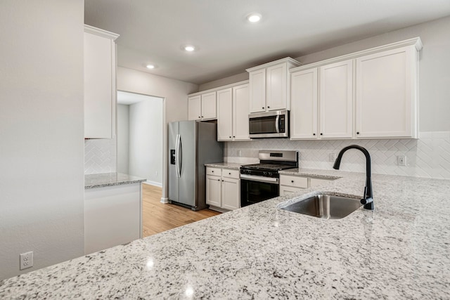 kitchen with stainless steel appliances, white cabinetry, sink, and light stone counters